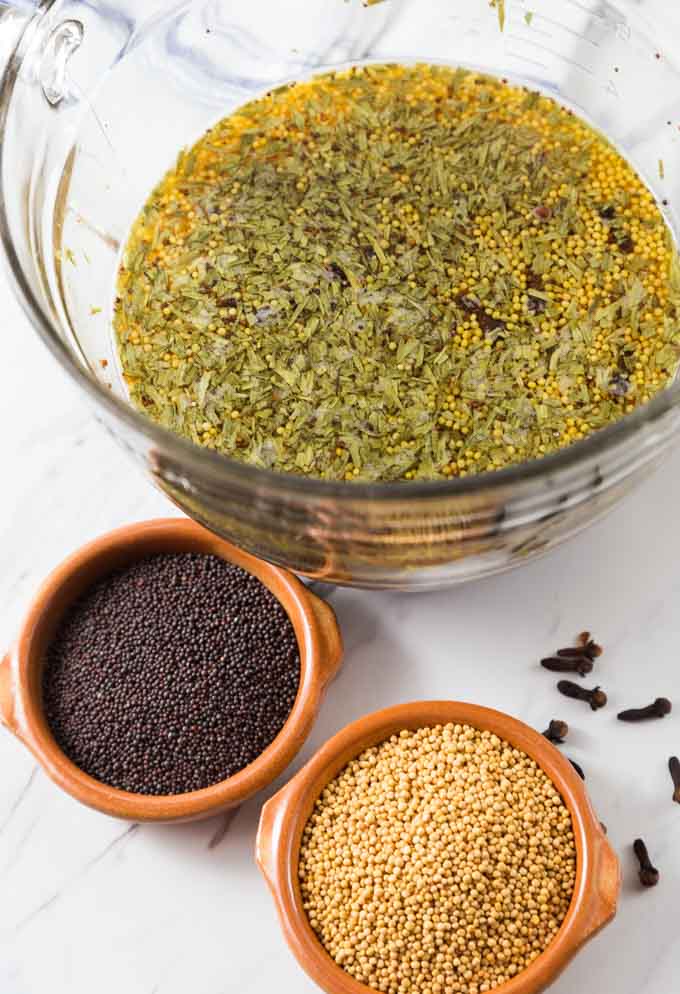 a bowl of water with mustard spiced soaking and two bowls of mustard seeds on the bottom