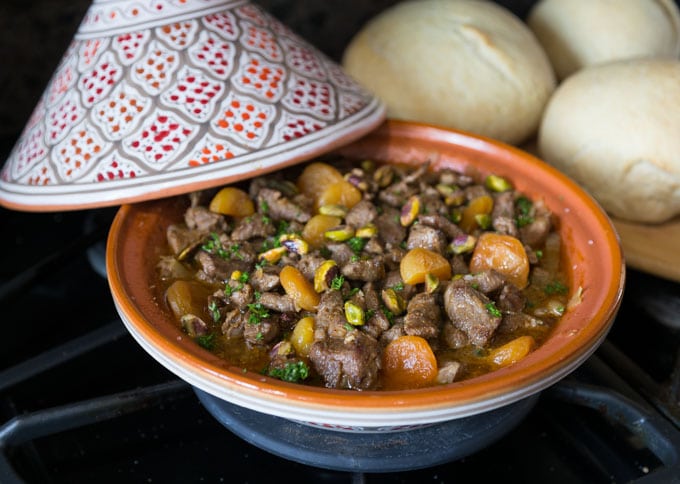 an orange tagine with cooked lamb, apricots, and carrots then bread in the back