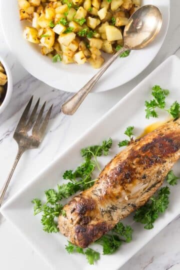 A photo of a cooked pork loin on a white platter with a bowl of apple maple chutney.