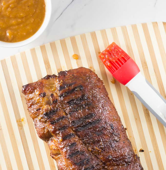 finished ribs on a cutting board with a bowl of sauce and a silicone brush on the right