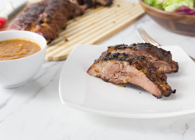 two finished bbq ribs on a white plate with sauce 