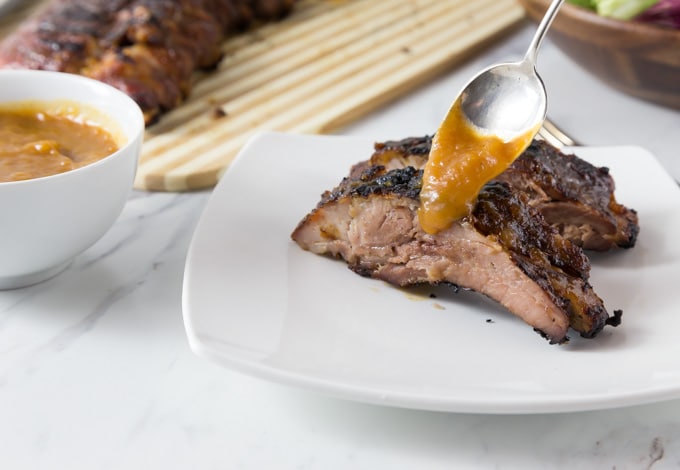 two bbq ribs on a plate with a spoon adding sauce