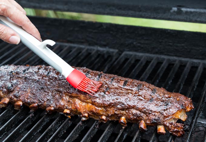 a rack of ribs on a grill with a brush spreading sauce
