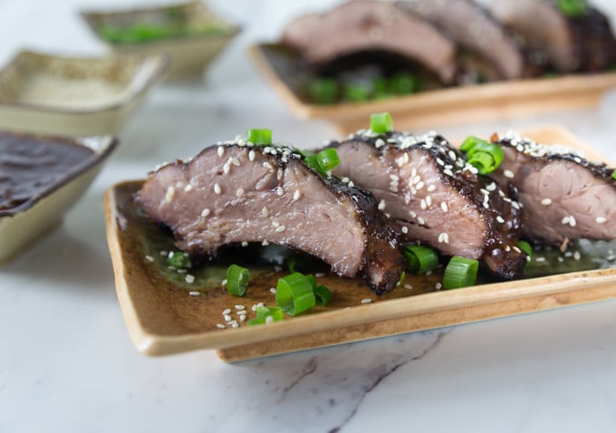 three bbq ribs on a plate with sesame seeds and green onions