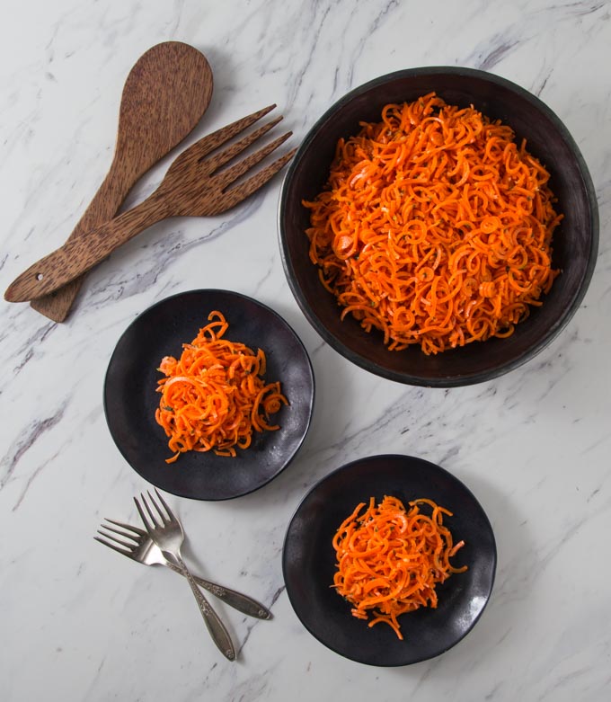 three black bowls of spiraled carrots with a wooden fork and spoon on the left