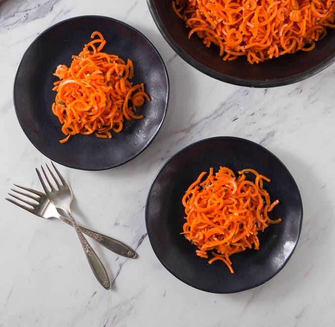 three black plates of spiralized carrots with two forks below 