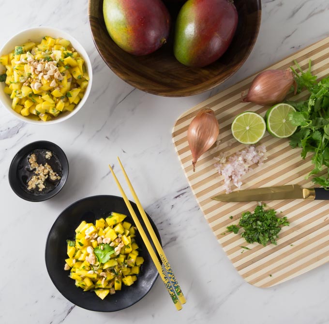 a bowl of vietnamese mango salad with chopsticks surrounded by chopped ingredients on a cutting board