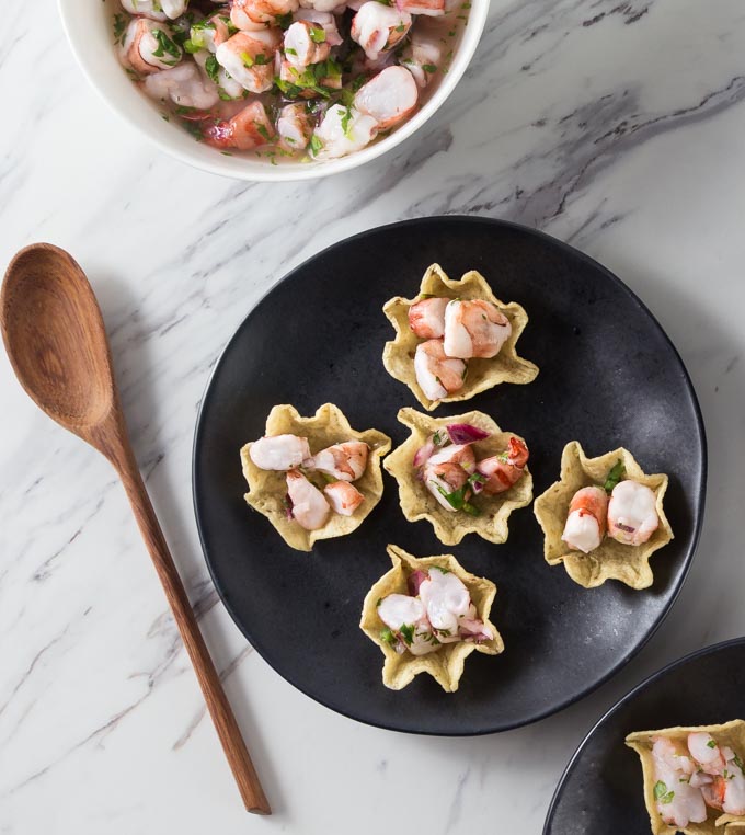 shrimp ceviche in chip bowls on black plate with wooden spoon