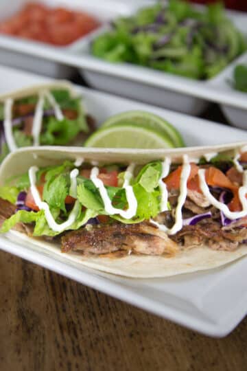 A photo of pork carnitas tacos on a white plate.