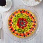 A French patisserie fruit tart on a clear platter with a cup of coffee and plates.