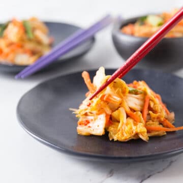 A photo of Korean kimchi on a black plate with red chop sticks.