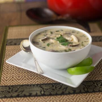 A bowl of Thai coconut soup on a plate with slices of lime.
