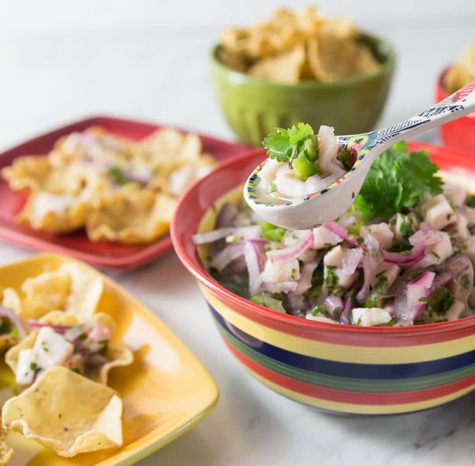 A photo of tilapia ceviche in a stripped bowl with chips and serving plates.