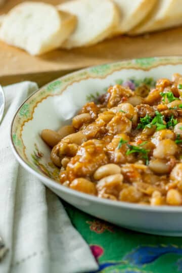 A photo of cassoulet in a bowl with a spoon and bread in the background.
