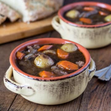 A photo of Guinness beef stew in a ceramic bowl with Irish soda bread in the background.
