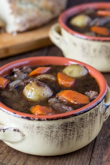 A photo of Guinness beef stew in a ceramic bowl with Irish soda bread in the background.