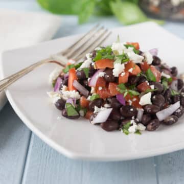 A photo of black bean tomato basil salad on a white plate with a fork.