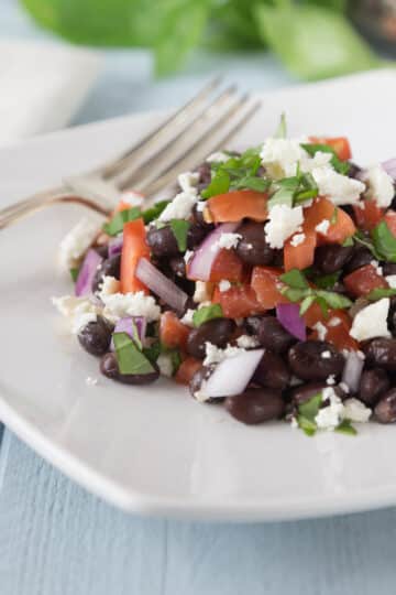A photo of black bean tomato basil salad on a white plate with a fork.