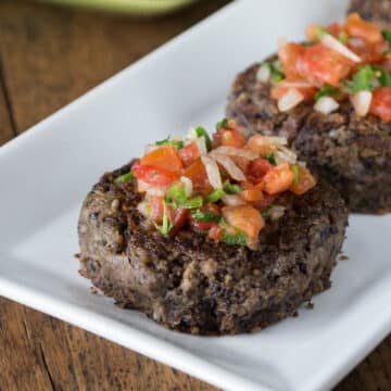 A photo of black bean burgers topped with pico de gallo on a white plate.