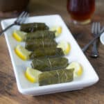 A photo of dolmas or dolmades on a white plate with lemon slices.