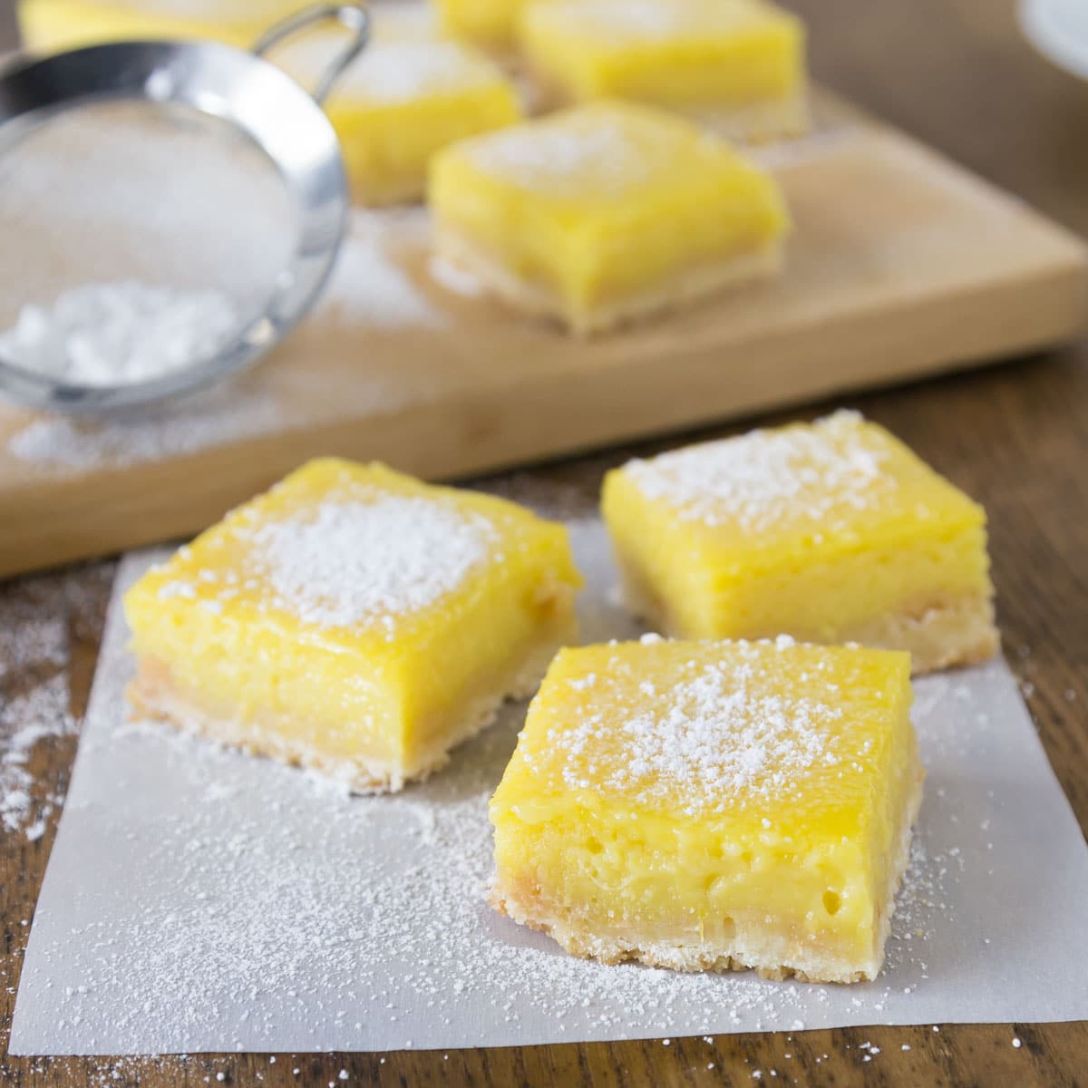 A photo of mango lime bars on parchment paper with powdered sugar.
