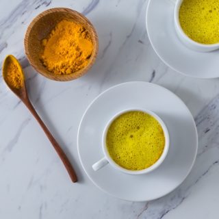 A photo of two white cups with turmeric and turmeric latte.