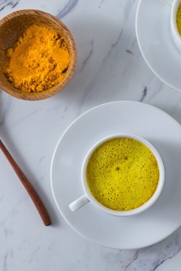 A photo of two white cups with turmeric and turmeric latte.