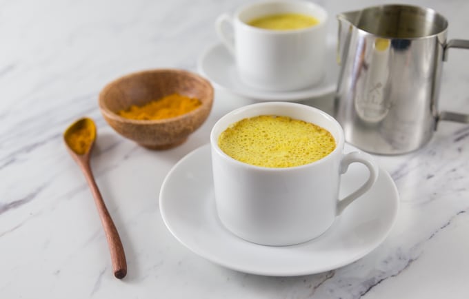 A photo of a white cup, frothing pitcher, turmeric and turmeric latte.