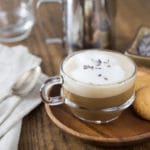 A photo of a clear coffee cup with lavender latte and some cookies.