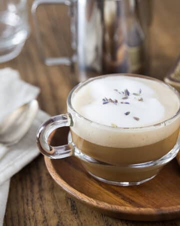A photo of a clear coffee cup with lavender latte and some cookies.