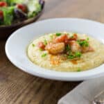A bowl with shrimp and grits and a salad in the background.