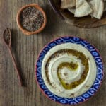 A bowl with hummus and za'atar with a wooden spoon.