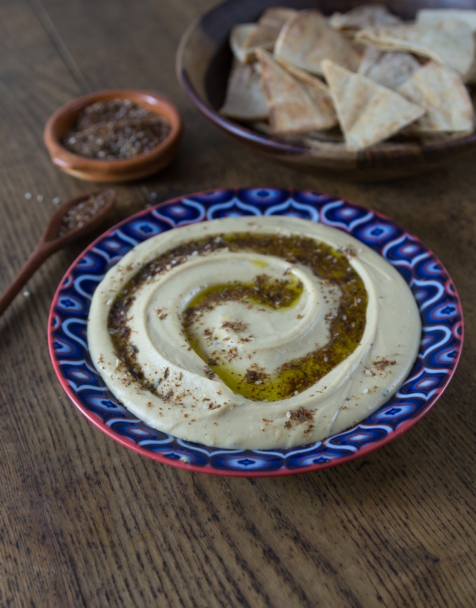 A blue bowl with hummus, pita and a wooden spoon with za'atar.