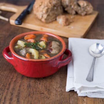 A photo of Dublin coddle in a red bowl with a napkin and spoon.