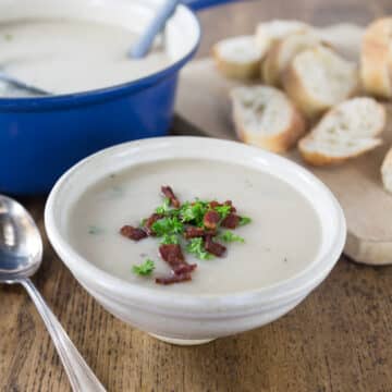 A bowl of Irish potato soup in a ceramic bowl with bacon and parsley on top.