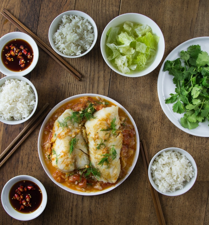 A large plate with Vietnamese tomato fish, a dish of soy sauce and rice bowls.