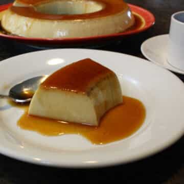 A photo of coconut flan on a white plate with a spoon.