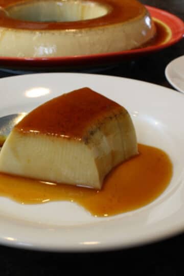 A photo of coconut flan on a white plate with a spoon.