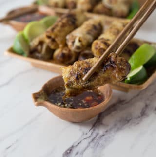 A photo of a Vietnamese spring rolls being dipped into sauce with chopsticks.
