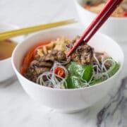A photo of bun thit nuong on a white bowl with noodles and greens.