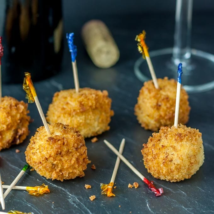 A photo of croquetas with toothpicks on a black plate.