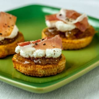 A green plate with a crostini, fig, ricotta and prosciutto.