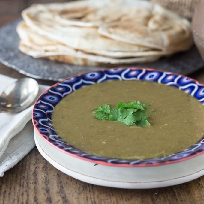 A photo of middle eastern lentil soup in a blue bowl with pita bread.