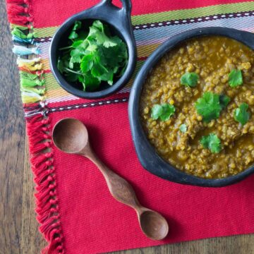 A photo of misir wot red lentil stew in a black bowl with cilantro.