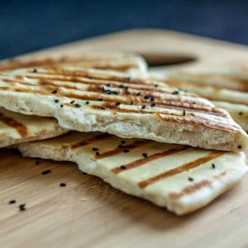 A photo of naan bread on a wooden cutting board.