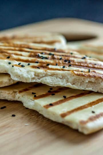A photo of naan bread on a wooden cutting board.