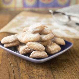 A photo of Spanish polvorones cookies on a blue plate with powdered sugar.