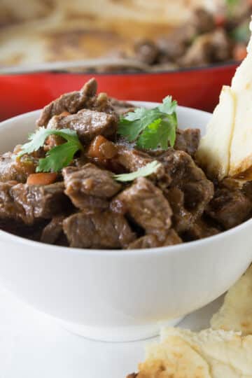 A photo of rogan josh in a white bowl with pita bread.