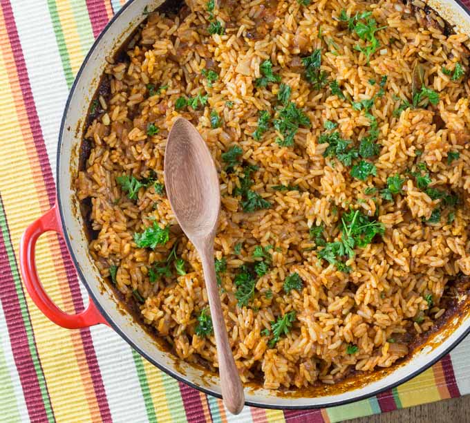 A photo of a large red pan with West African jollof rice and a wooden spoon.