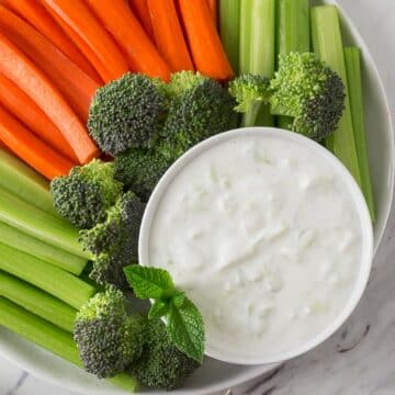 An overhead photo of a bowl of tzatziki with celery, carrots and broccoli.